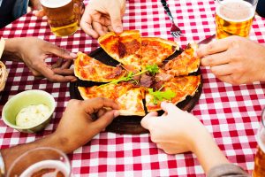 Several hands reaching for a slice of pizza